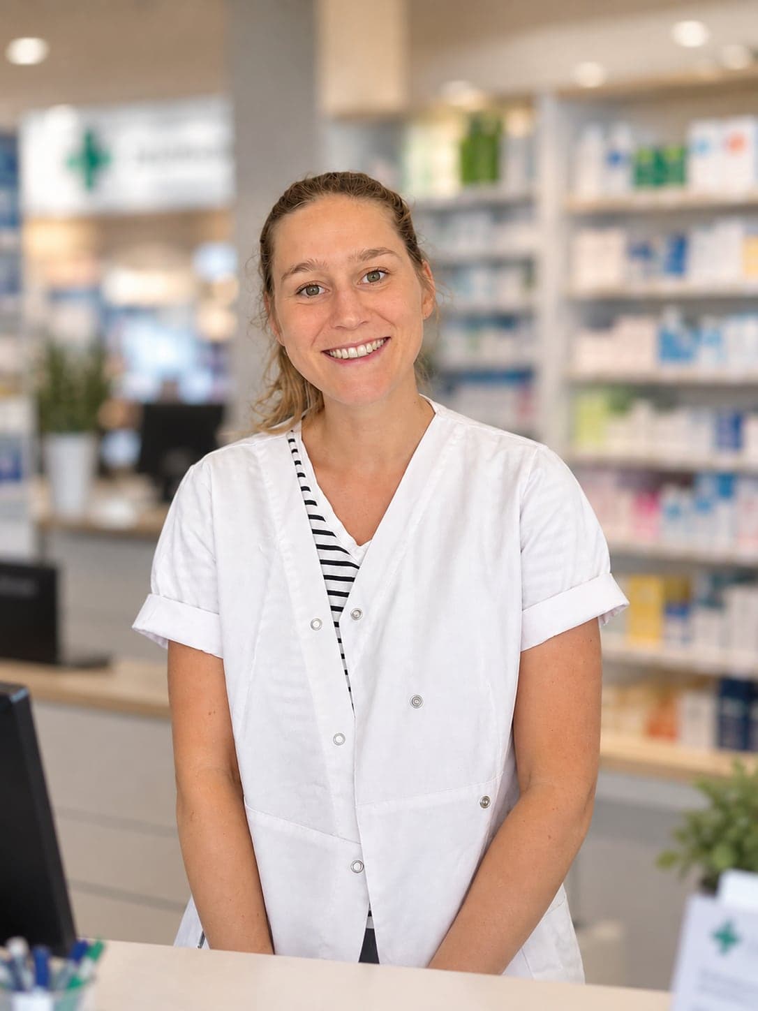 Clémence, souriante, en blouse blanche derrière le comptoir de sa pharmacie